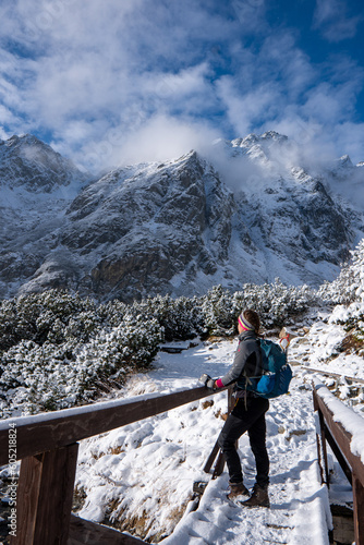Obraz na płótnie Hiker woman standing on the bridge and looks around, admiring winter mountain landscape. Happy tourist woman in winter. High Tatras, 1987 meter above sea level. Slovakia w salonie