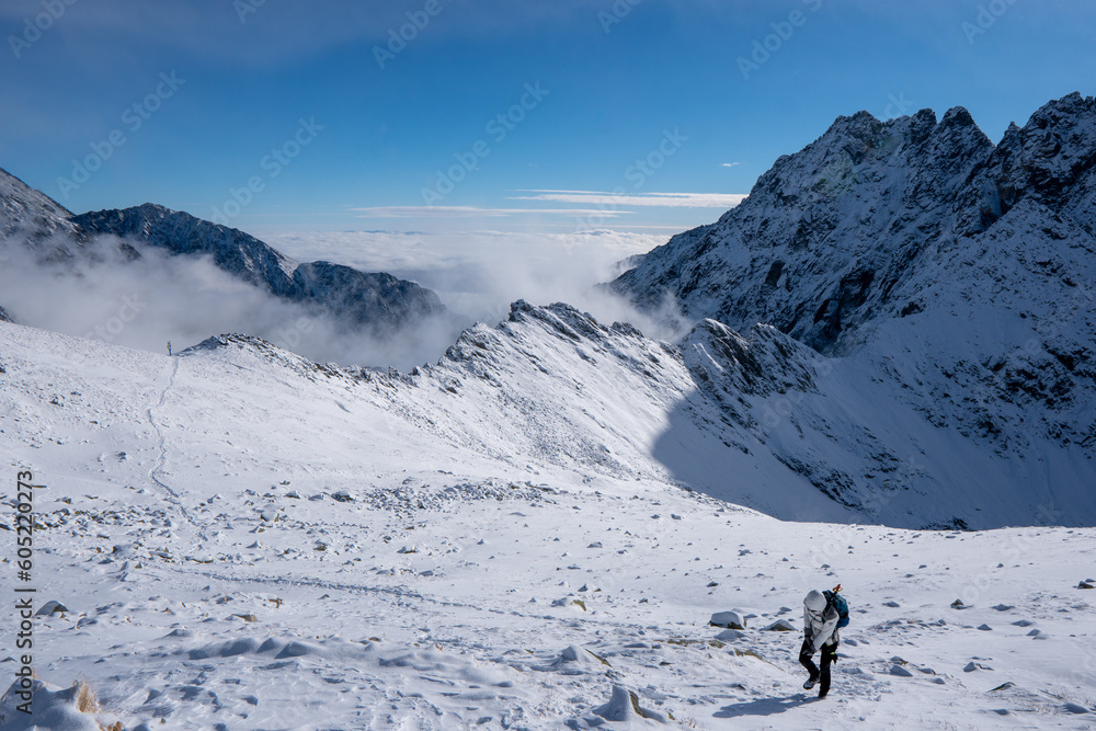 Hiker woman standing and looks around, admiring winter mountain landscape. Happy tourist woman in winter. High Tatras, 1987 meter above sea level. Slovakia