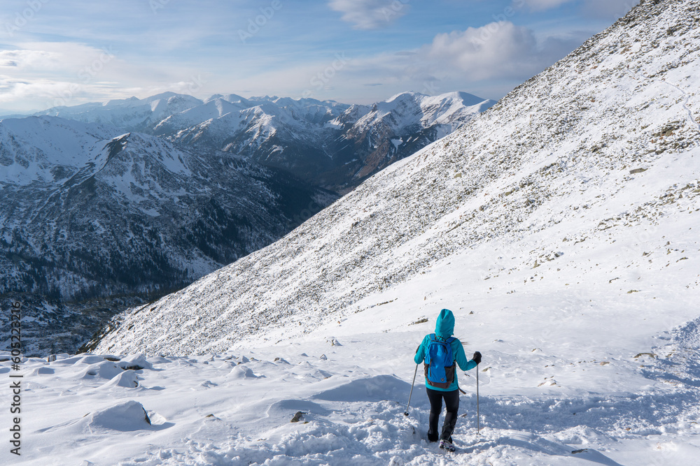 Adventurous women hiker on top of a steep rocky cliff overlooking winter alpine like moutain landscape of High Tatras, Slovakia.