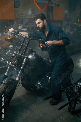 Auto mechanic pushing motorcycle on repair stand in workshop garage © Nomad_Soul
