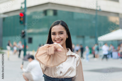 Принти на полотні A pretty asian woman standing outside wearing a light tan silk blouse and a high waist skirt, pointing directly at the camera while smiling