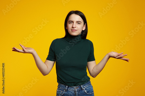 Clueless and careless cute caucasian girl dont know anything  shrugging with reluctant face  standing against yellow background