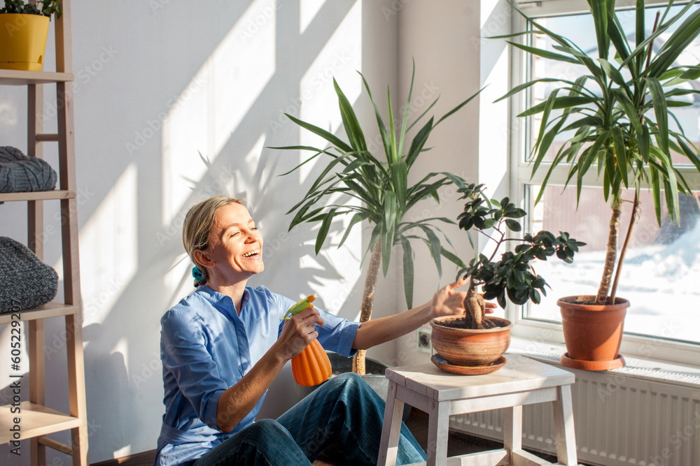 Middle aged woman sprays plants in flowerpots at home Middle aged woman sprays plants in flowerpots at home