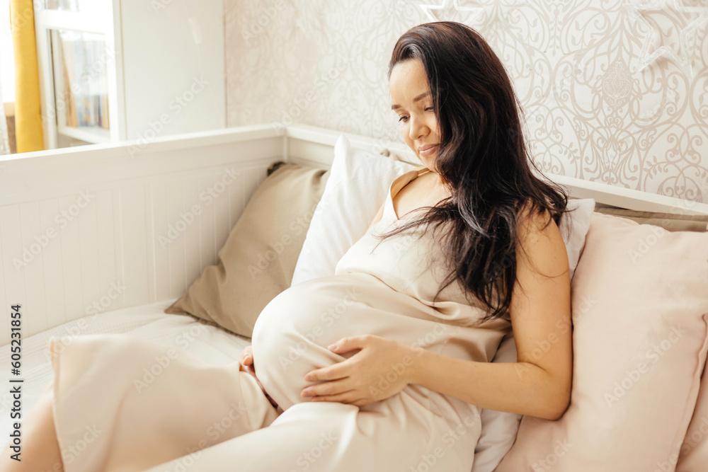 A beautiful pregnant girl strokes her stomach and listens to music in a home interior. A beautiful pregnant girl strokes her stomach and listens to music in a home interior.