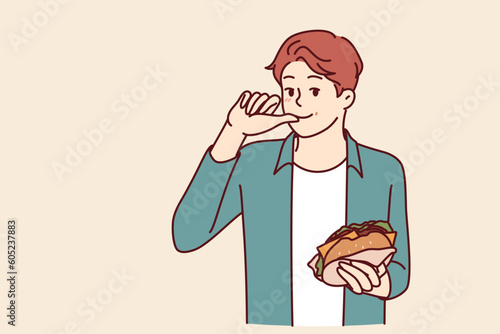Man with burger licks fingers and enjoys reception of fast food bought in street restaurant or ordered for delivery. Smiling guy holding tasty cheese burger while eating sandwich with cutlet