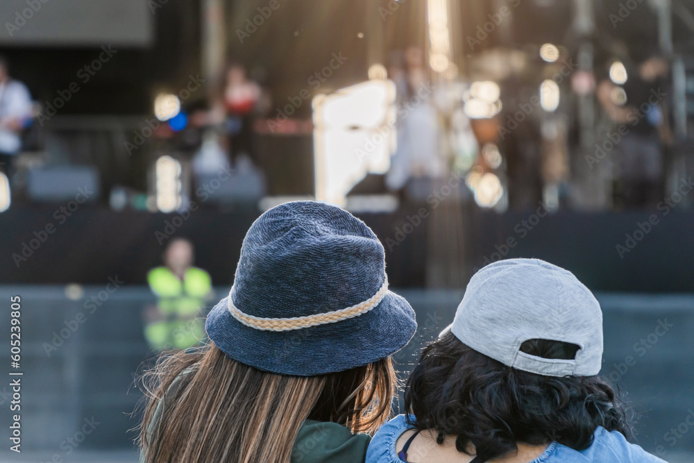 Friends with hats statying in front of a summer music festival stage. Waiting for the concert to start