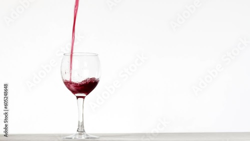 Red wine is being poured into a glass on the white background photo