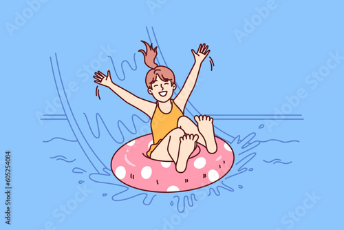 Little girl in pool floats on inflatable ring and enjoys visiting aqua park in sunny summer weather. Happy childhood of child relaxing in pool and sliding down slide in water park for kids