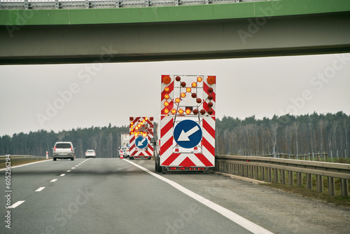 Truck arrow down left reflective direction road sign. roadwork on the one of the lanes. A truck with an arrow on the back is driving down a highway