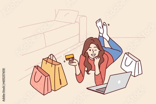 Woman with credit card and laptop after internet shopping or ordering goods on website of popular online store. Girl lying on floor and winking invites to shopping using bank card with cashback