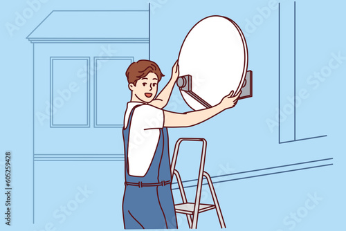 Master installs television satellite dish on facade of building standing on stepladder and looking at screen. TV company specialist sets up access to satellite TV channels for residents house