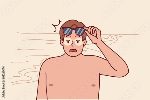 Tanned man takes off sunglasses and screams after getting sunburn relaxing on beach. Funny guy tanned during trip to resort and needs cream to protect against sun rays and ultraviolet radiation