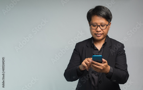 Portrait of a businesswoman with short black hair using a smartphone with a smile while standing on a gray background