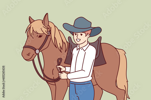 Cowboy boy is standing next to horse caring for stallion and wanting to become professional jockey and race. Schoolboy wearing texas ranger hat near horse for ride or competition at racetrack