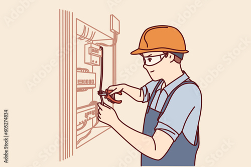 Man electrician repairs power shield and connects residential building or factory to electricity. Guy in electrician uniform repairs wiring standing near cabinet with power machines and wires