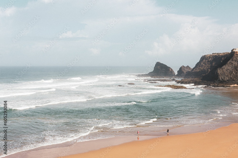 Top view of two people standing at the beach while the foamy shallow sea waves approach the coast