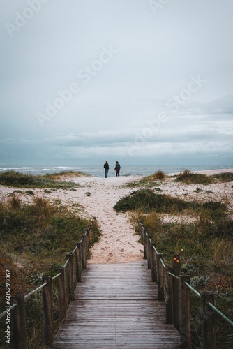 Vertical of two people standing on the beach and enjoying the view of the tranquil seascape