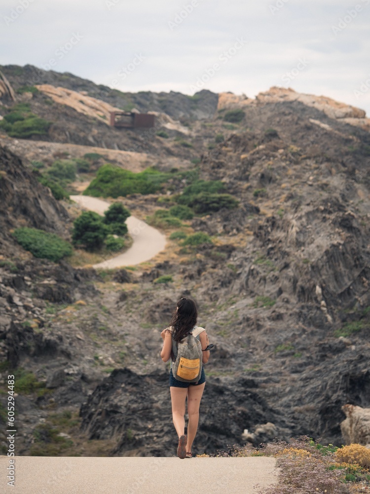 Naklejka premium Aerial view of female walking through road in background of rocky mountains in Cap de Creus