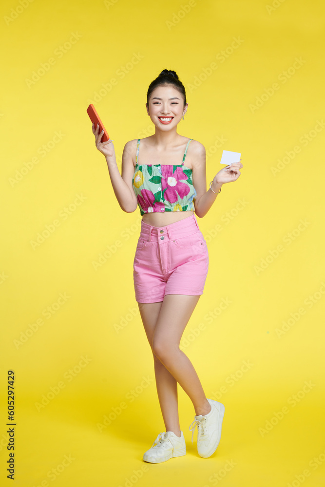 Portrait of a smiling woman holding credit card and mobile phone over yellow background Portrait of a smiling woman holding credit card and mobile phone over yellow background