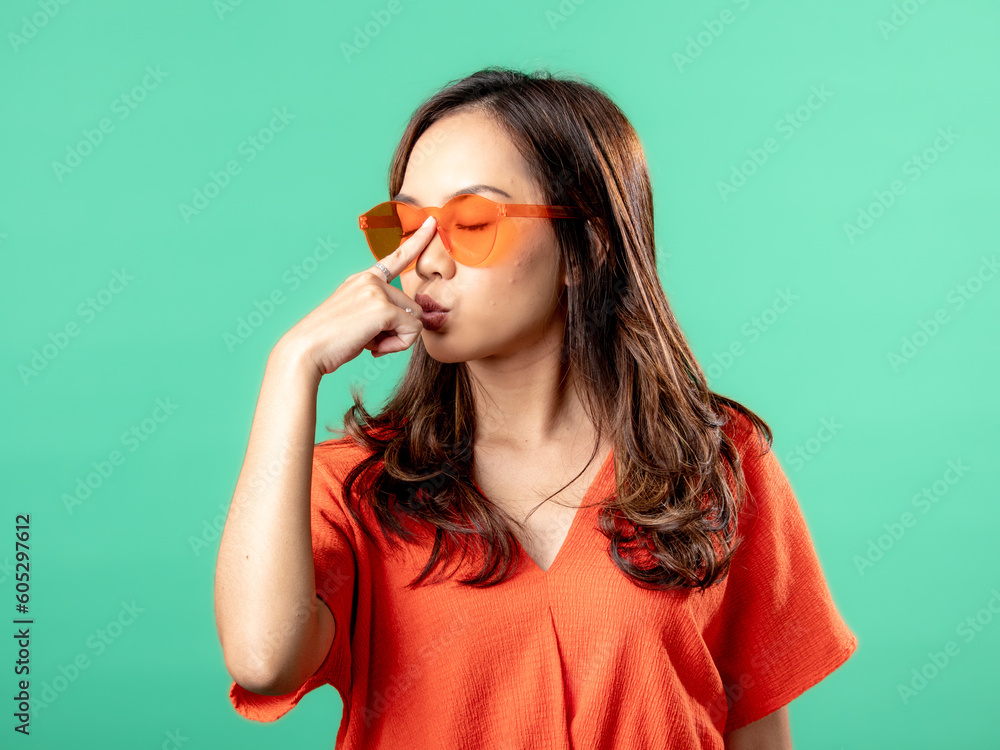 A portrait of an Asian woman wearing an orange shirt and glasses, holding her glasses, isolated on a green background. A portrait of an Asian woman wearing an orange shirt and glasses, holding her glasses, isolated on a green background.