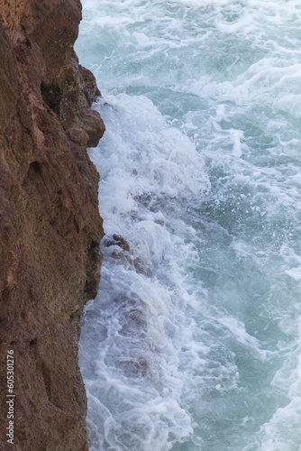 Aerial shot of the shore covered with rocky mountains and waves of water in the background