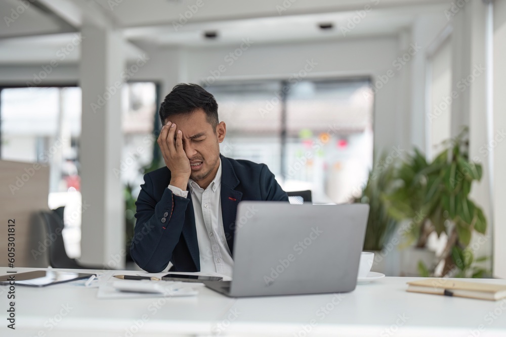 Tired exhausted business man office worker sitting at his desk tired of working in a laptop, overworked, having a headache, closed his eyes, needs rest and break Tired exhausted business man office worker sitting at his desk tired of working in a laptop, overworked, having a headache, closed his eyes, needs rest and break