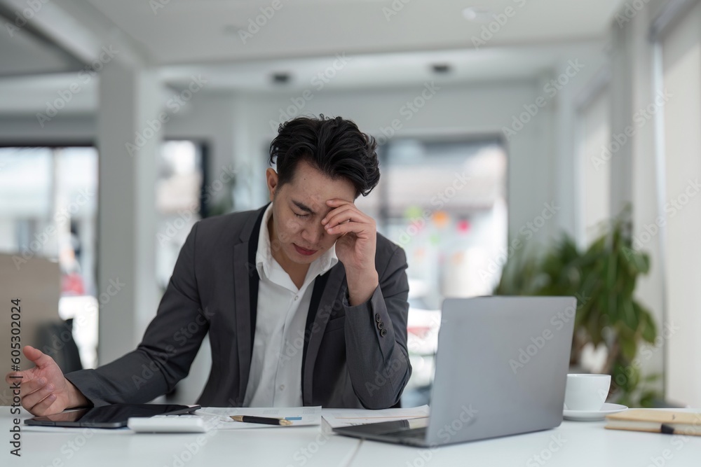 Tired exhausted business man office worker sitting at his desk tired of working in a laptop, overworked, having a headache, closed his eyes, needs rest and break Tired exhausted business man office worker sitting at his desk tired of working in a laptop, overworked, having a headache, closed his eyes, needs rest and break