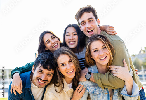 Diverse group of friends smile at camera outdoors. Multiethnic young people having fun together. Millennial men and women enjoying summer travel. Friendship and youth community concept.