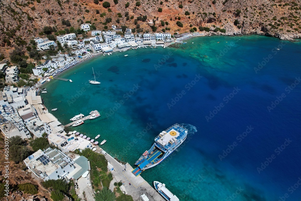 Bird's eye view of the greenish-blue sea with boats and white buildings of Loutro. Crete, Greece.