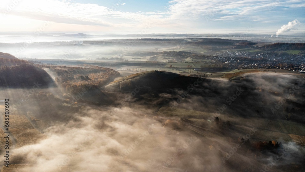 Obraz premium Aerial shot over a village and cultivated lands covered in fog at a sunny sunrise