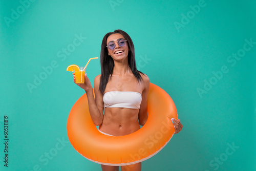Photography Positive woman with inflatable ring, holding tropical cocktail on blue background