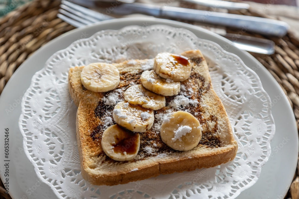 Horizontal closeup of freshly cut bananas, chocolate and sugar powder on toast on a wooden table
