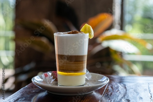 Horizontal selective focus of a barraquito shot on a brown wooden table with a lemon peel in it photo