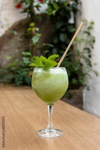 Vertical shot of a glass with a delicious fancy iced green mint cocktail in a garden bar