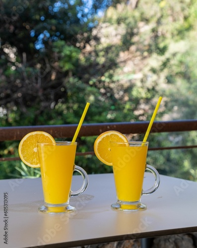 Vertical shot of fancy glasses of freshly squeezed orange juice with an orange slice and a straw
