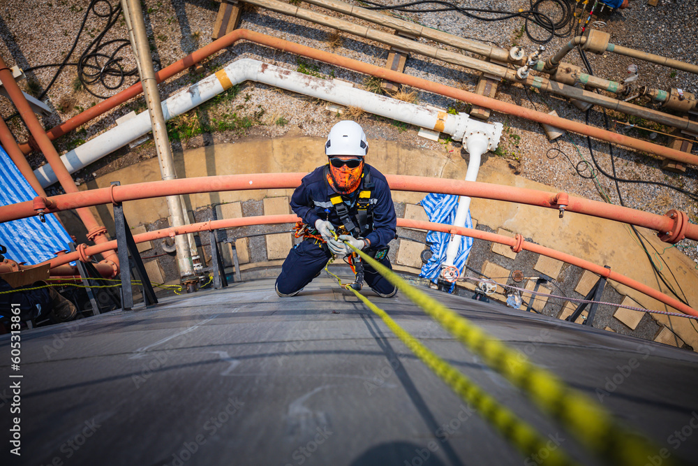 Naklejka premium Focus top view male worker down height tank roof rope access safety inspection of thickness storage tank .