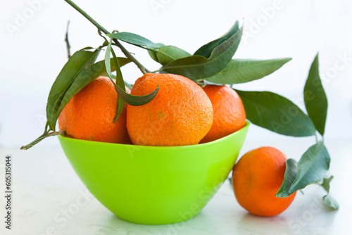 Ripe juicy tangerines with twigs and leaves in a bowl