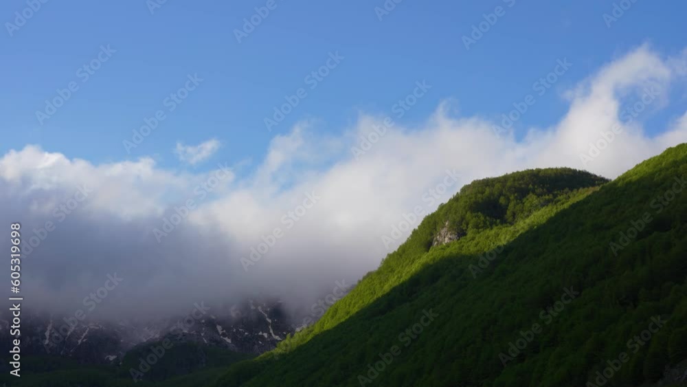 White Clouds Streaming Across Lush Greenery and Rocky Slopes in the Majestic Alps, under a Blue Sky, During the Enchanting Spring Sunrise White Clouds Streaming Across Lush Greenery and Rocky Slopes in the Majestic Alps, under a Blue Sky, During the Enchanting Spring Sunrise