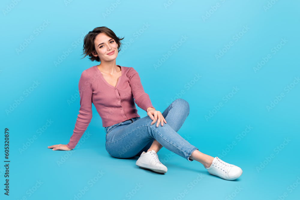 Full size portrait of adorable satisfied girl sit floor have good mood isolated on blue color background Full size portrait of adorable satisfied girl sit floor have good mood isolated on blue color background