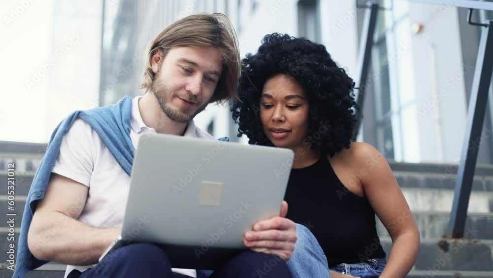 Smiling young interracial couple looking at laptop computer screen choose products in online internet store make order online booking or plan trip at city Happy people enjoying time together outdoors Smiling young interracial couple looking at laptop computer screen choose products in online internet store make order online booking or plan trip at city Happy people enjoying time together outdoors