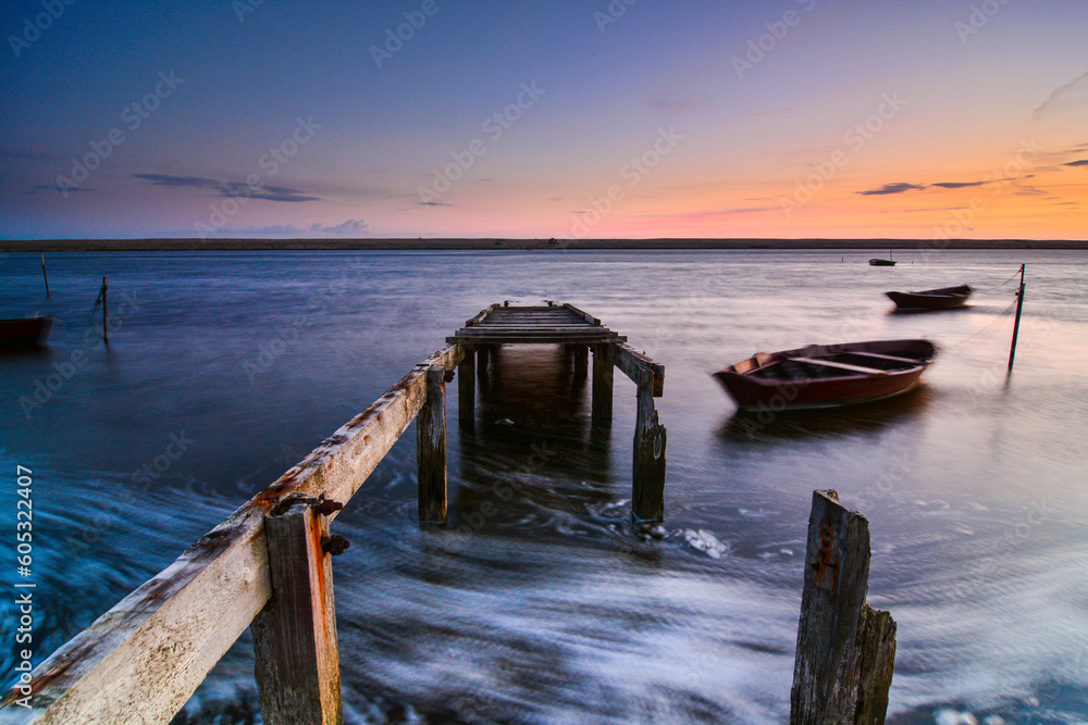 Sea scene with jetty, boats at sunset.