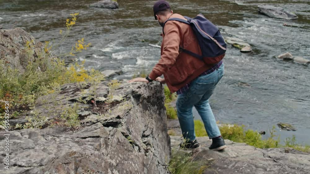 Tilt shot of young male Biracial tourist going down rock cliff near to river Tilt shot of young male Biracial tourist going down rock cliff near to river