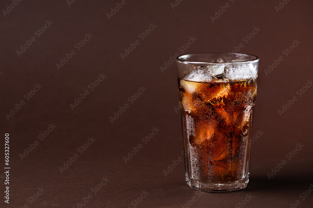 A glass of cola drink with ice cubes. Fresh cold sweet cola drink with ice one brown background with copy space. A glass of cola drink with ice cubes. Fresh cold sweet cola drink with ice one brown background with copy space.