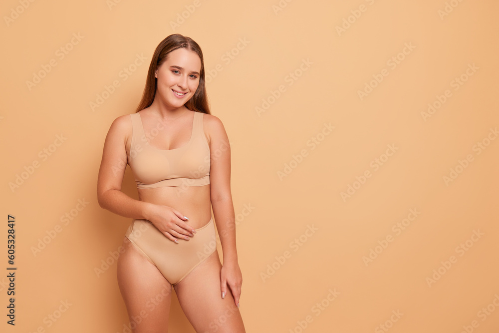Half-nude girl in beige underwear looking at camera with smile posing on  peach colour studio background, comfortable underclothing concept, copy  space Stock Photo