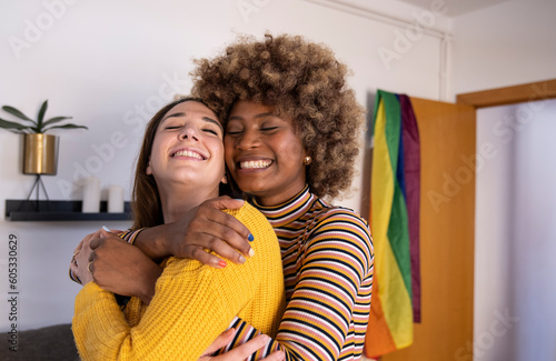Leinwand Poster Beautiful and cheerful multiracial lesbian couple hugging at their apartment
