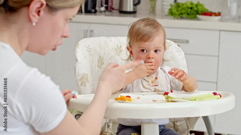 Little cute baby girl sitting at feeding table and eats vegetables
