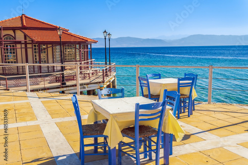 Empty tavern restaurant by the seafront with wooden chairs and tables under a bright sun in summer.