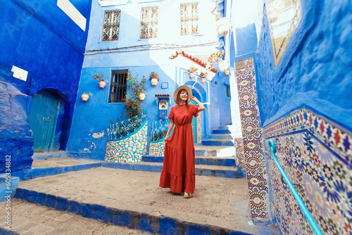 Young woman with red dress visiting the blue city Chefchaouen, Marocco - Happy tourist walking in Moroccan city street - Travel and vacation lifestyle concept