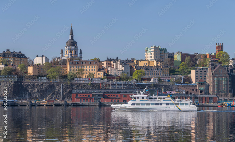 A modern commuting ferry leaving for the archipelago passing the cliffs of the district Södermalm part 
Sofo, a tranquil sunny summer day in Stockholm