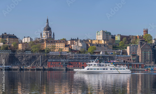 A modern commuting ferry leaving for the archipelago passing the cliffs of the district Södermalm part  Sofo, a tranquil sunny summer day in Stockholm © Hans Baath
